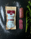Sauccisson sec packaging with sliced salami and rosemary on a black surface