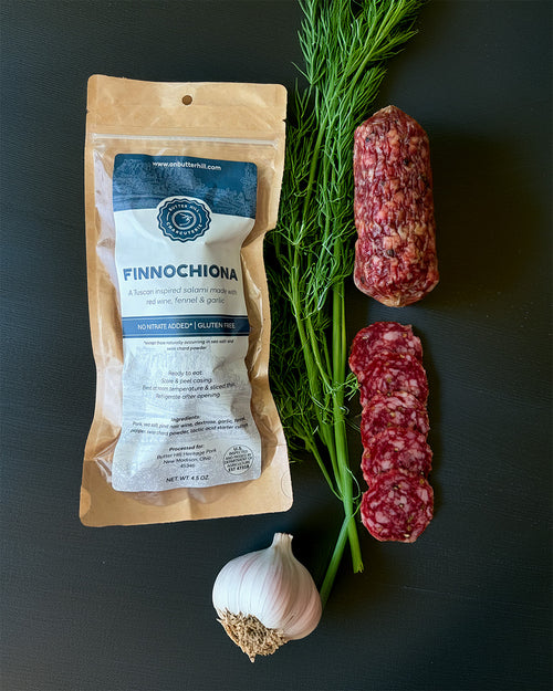 Packaged salami with a sprig of dill and garlic on a dark surface