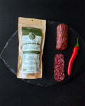Soppressata package with sliced salami and a red chili pepper on a black slate surface
