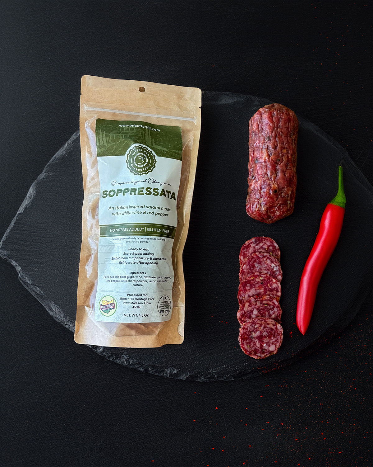 Soppressata package with sliced salami and a red chili pepper on a black slate surface