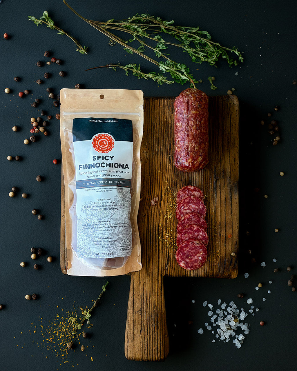 Spicy Finnochiona salami on a wooden board with packaging and spices on a dark background