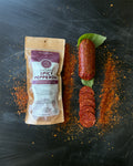 Spicy pepperoni packaging with pepperoni slices and a whole pepperoni on a dark surface